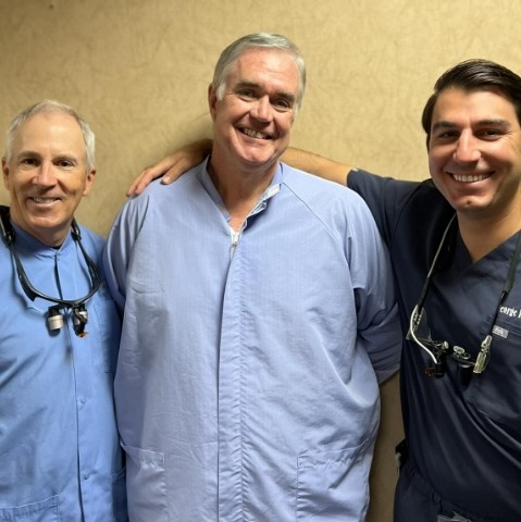 Three smiling Rock Hill dentists in front of yellow wall