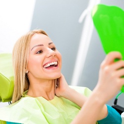 Woman smiling while sitting in dental chair holding green mirror