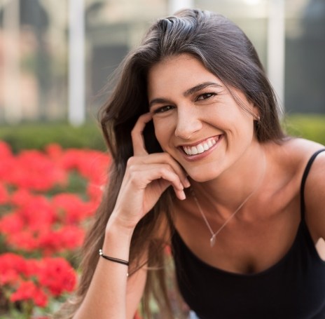 Young woman smiling in front of bush with red flowers