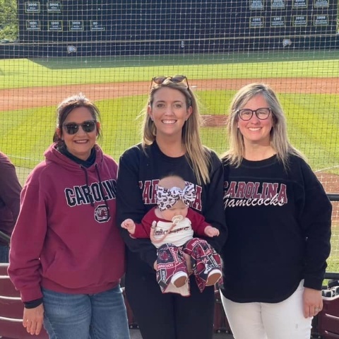 Three smiling dental team members in stands at baseball game