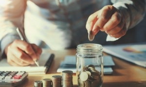 Person using calculator while placing coins in a glass jar