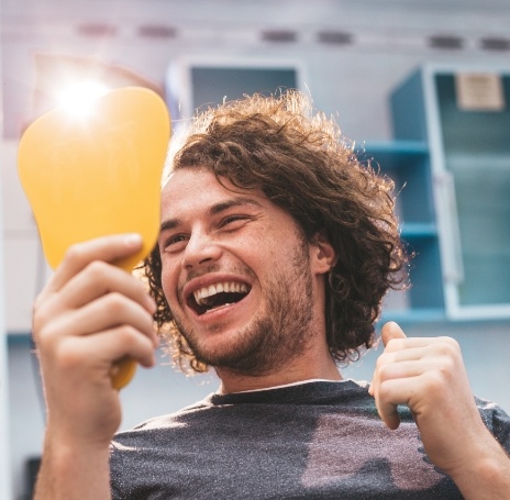 Young man in dental chair looking at his smile in mirror