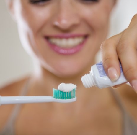 Person putting toothpaste on an electric toothbrush