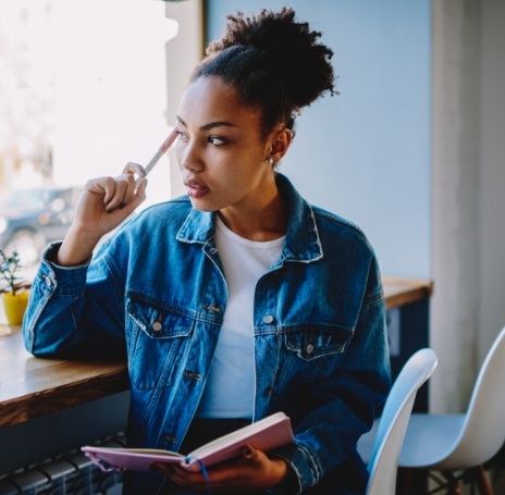 Woman in denim jacket sitting at desk with notebook and pen