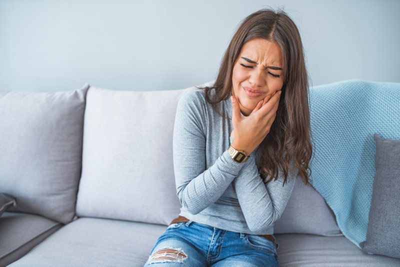Woman on couch with tooth pain from an interproximal cavity