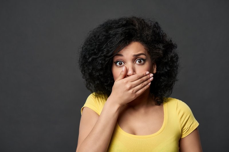 A woman covering her mouth after her dental bridge fell out