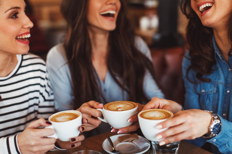 Patient smiling with friends over a cup of coffee after tooth extraction